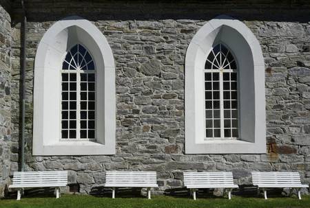 Zwei Kirchenfenster von außen mit vier Bänken davor